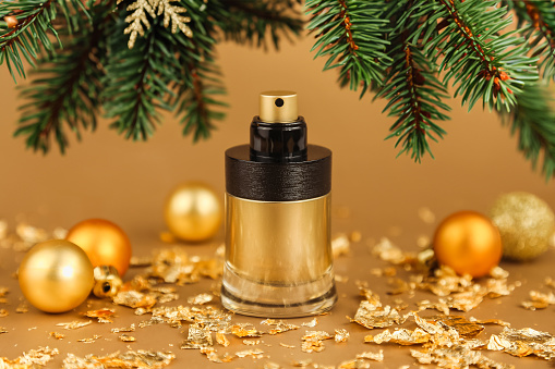 perfume spray gold black bottle, christmas balls, pieces of gold paper, green fir tree on golden background. mockup, eau de toilette, front view
