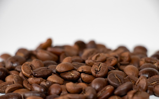 Heap of dark coffee beans on the white surface. Close up photo. Selective Focus.