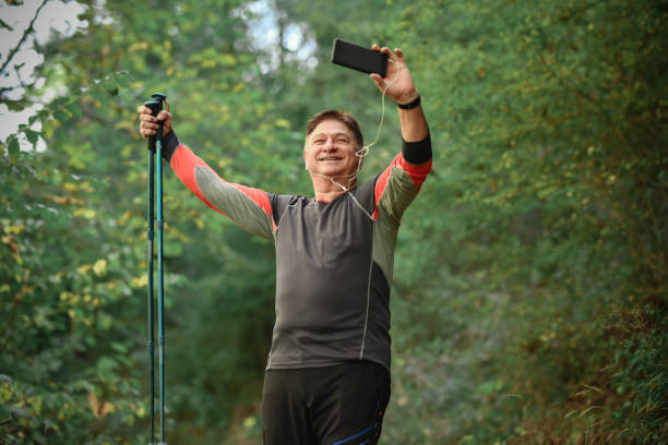 randonneur masculin senior prenant un selfie tout en traversant de belles terres boisées - pointer stick audio photos et images de collection