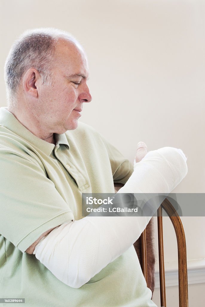 Uomo maturo con un braccio rotto nel cast seduta - Foto stock royalty-free di Braccio rotto
