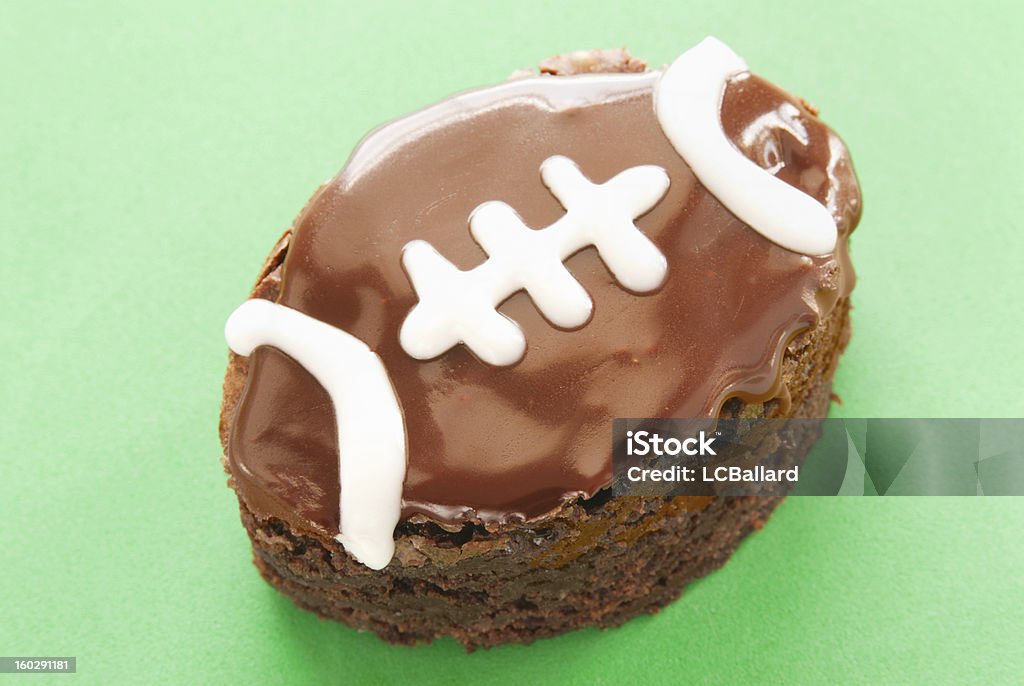 chocolate brownie shaped and decorated like a football green background homemade dark chocolate brownie shaped like a football. This sweet food has chocolate icing and white piping for the footballs trim. The background is green textured paper.  American Football - Sport Stock Photo