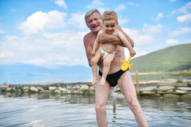 자랑스러운 할아버지는 아기를 해변으로 데려가 그와 함께 즐거운 시간을 보냅니다 - grandson water waterfront portrait 뉴스 사진 이미지
