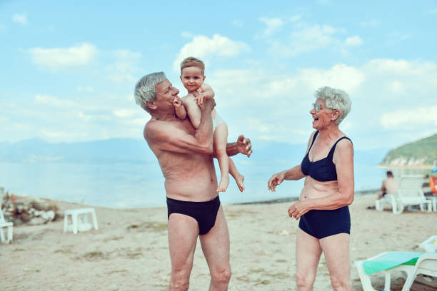 할아버지가 해변에서 아기 손자를 들어 올리고 껴안고 있다 - grandson water waterfront portrait 뉴스 사진 이미지