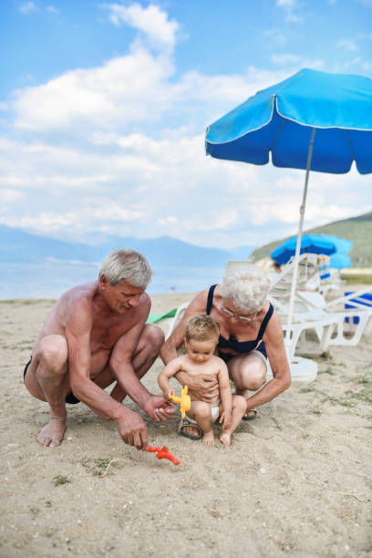 아기가 해변에서 모래성을 만드는 것을 돕는 조부모 - grandson water waterfront portrait 뉴스 사진 이미지