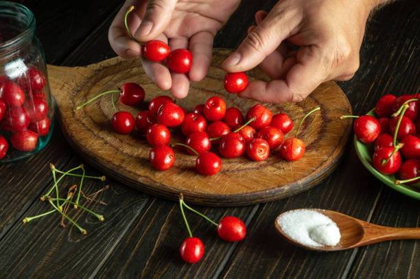 istock Preparation of fruit drink from fresh cherries. Cook's hands sorting cherry berries before preparing a sweet drink in a jar 1602941818