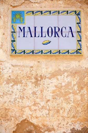 A hand painted Spanish tiled sign panel with painted Majorca text with a leaf motif border, inset into a distressed paint wall on the island of Majorca in the Balearic Islands, in the Mediterranean. Good copy space.