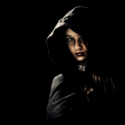 Teenage girl wearing a dark cape, looking at camera. Isolated on black.