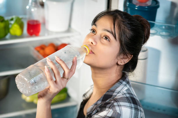 istock Woman drinking cold water while standing front of fridge in hot summer. 1602990266