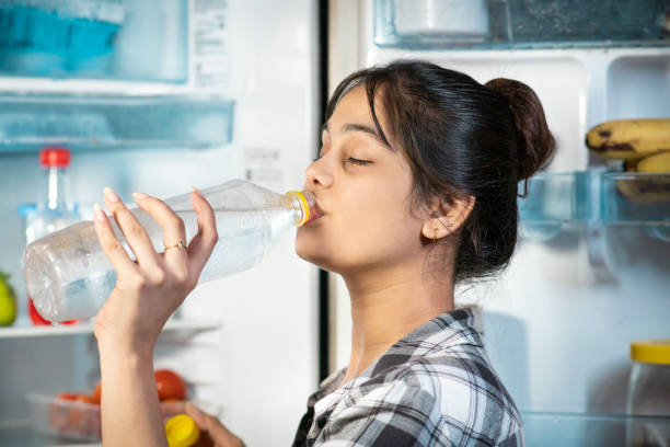 istock Woman drinking cold water while standing front of fridge in hot summer. 1602990457