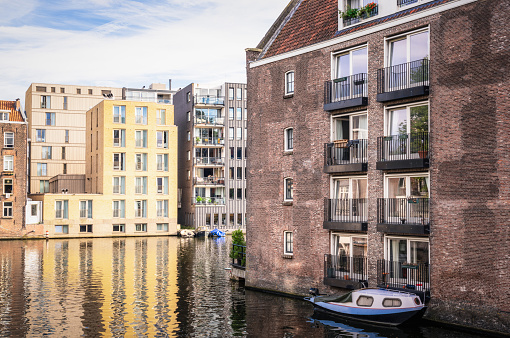A small boat moored by a modern, brick built apartment building in central Amsterdam.