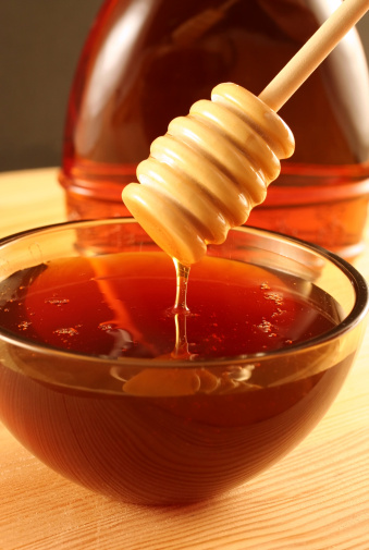 A vertical image of a honey dripper drizzling wild, natural honey into a bowl