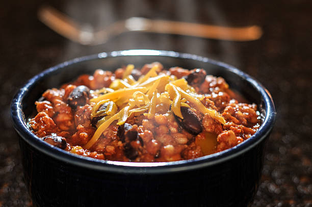 Chili con carne with cheese in a bowl A steamy bowl of Chili topped with chedder cheese with a fork in the background chili con carne photos stock pictures, royalty-free photos & images