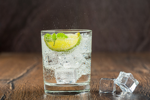 Refreshing mineral water in a glass with ice cubes, mint leaves and lime slice. Spray over a glass of water. Wooden background.