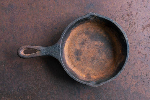 Old rusty round cast iron frying pan on old rusty background, view from above