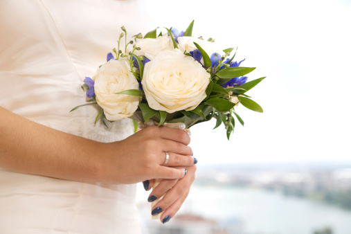 Bride with bridal bouquet, holding it in front of her waist, blurred landscape in the background.