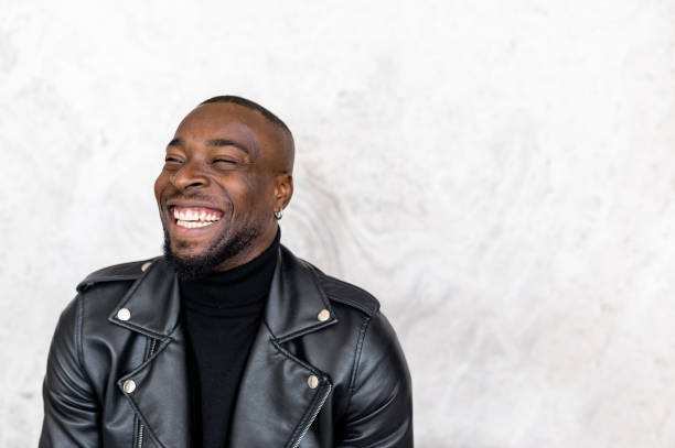 Delighted African American male in stylish leather jacket looking away and smiling happily