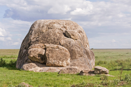 Huge field stone in savanna against cloudy sky background. Serengeti National Park, Great Rift Valley, Tanzania, Africa. 