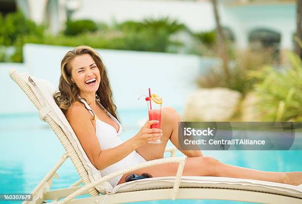 Foto de Sorrindo Jovem Mulher Em Traje De Banho Relaxante Com Um Coquetel Na Chaiselongue e mais fotos de stock de Adulto