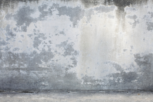 Image with extreme detail of a rustic, concrete wall with many different colored stains and paint. Image includes where the wall meets the concrete ground.