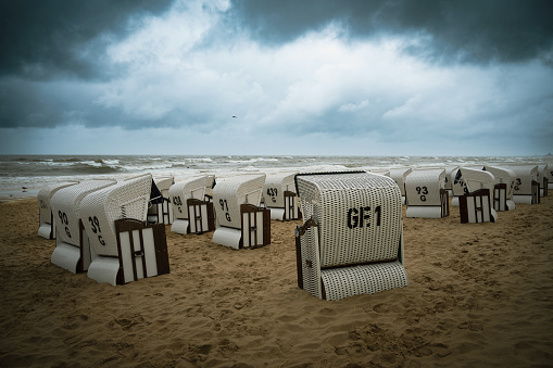 Roofed wicker beach chairs at the baltic sea beach, coast at the island of Usedom in Germany, storm and rain over the brack water, high waves, storm warning