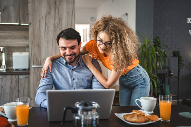 istock Lovely girlfriend hugging her boyfriend while he is working on laptop, eating breakfast and drinking coffee 1603118589