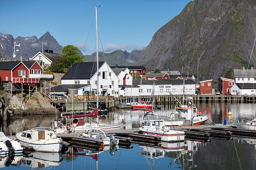Reine, Norway - July 12 2023: A sailing boat anchored in front of the wooden Rorbu cabins in the Lofoten Islands fishing village Reine