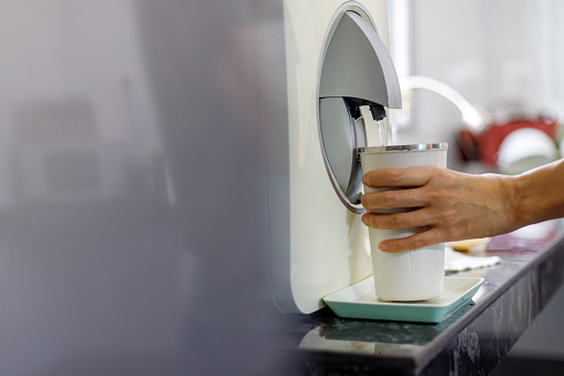 A hand holding a water tumbler, filling it with hot water from a water dispenser.