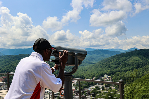 A portrait of a black man looking at mountains through coin-operated viewing telescopes