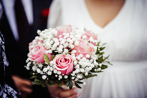 Gold wedding rings and bouquet from white roses on a background of blurred newlyweds
