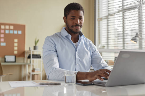 istock Handsome black businessman using laptop  working at desk in office and smiling 1603179609