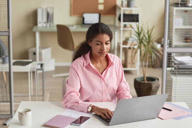 Black young woman wearing pink in office  using computer