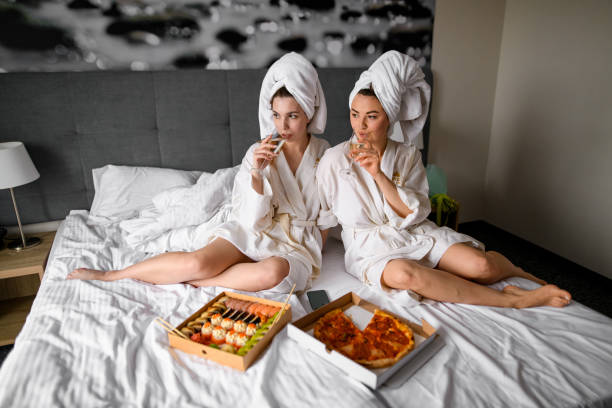 dos hermosas mujeres en batas de baño disfrutan de champán y comida en el hotel - two party system fotografías e imágenes de stock
