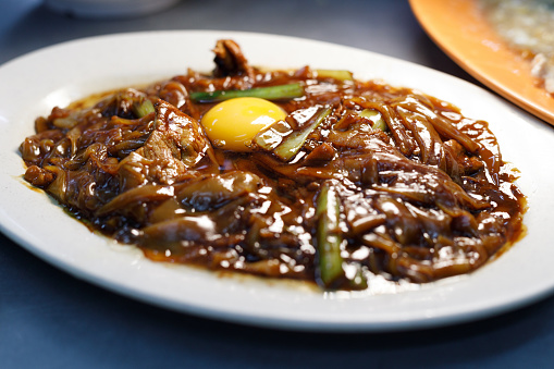 Stir-fried rice noodles with pork meat and raw egg in dark soy sauce also know as Char Hor Fun, Malaysian Chinese popular street food in Ipoh state.
