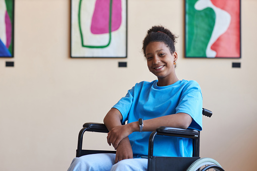 Colorful portrait of black teenage girl with disability smiling at camera while visiting modern art gallery or museum, copy space