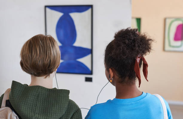 back view two teenagers in  art gallery sharing earphones with audio guide - museum child art museum art imagens e fotografias de stock