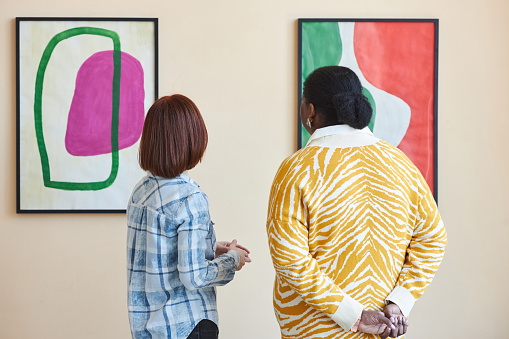Colorful back view of two people looking at abstract art painting in modern art gallery or museum