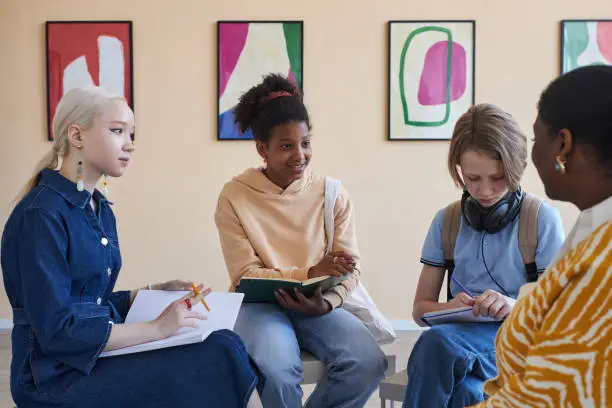 Photo of Teenagers sitting in circle and taking notes while discussing art in modern art