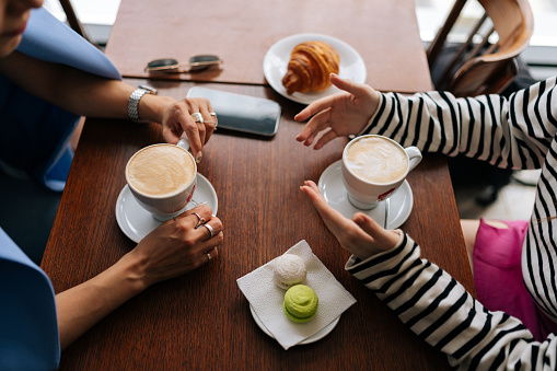 Close-up high-angle view of unrecognizable two happy female girlfriends sharing news, planning weekend, enjoy pleasant warm conversation resting indoor siting at table by window in coffee shop.