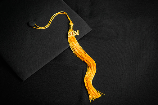 A class of 2024 charm on a yellow tassel on a black background.