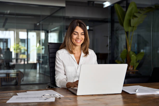 istock 40s mid age European business woman CEO using laptop application for work sitting at table workspace in office. Smiling Latin Hispanic mature adult professional businesswoman using pc digital computer 1603220496