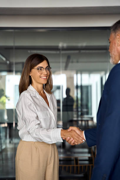 Mature Latin business team of woman and European business man shaking hands as colleagues, partners or employees, signing a contract. Group of people satisfied with results of team work, vertical shot stock photo