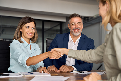 Mature Latin business team of woman and European business man shaking hands with colleagues, partners or employees, signing a contract. Group of people satisfied with results of team work together.