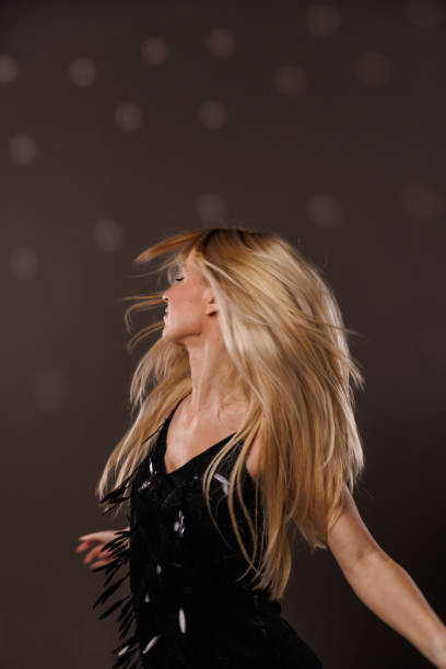 Portrait of cool young blond woman having fun and enjoying dancing against gray background with disco ball throwing reflection on her. Her hair flying all over due to dancing.