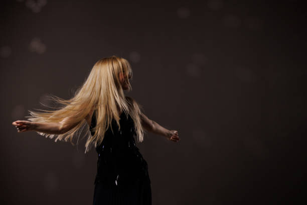Portrait of cool young blond woman having fun and enjoying dancing against gray background with disco ball throwing reflection on her. Her hair flying all over due to dancing.