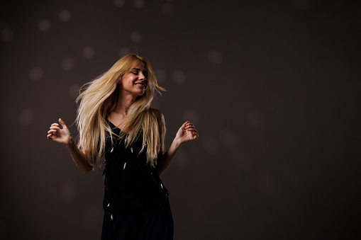 Portrait of cool young blond woman having fun and enjoying dancing against gray background with disco ball throwing reflection on her. Her hair flying all over due to dancing.