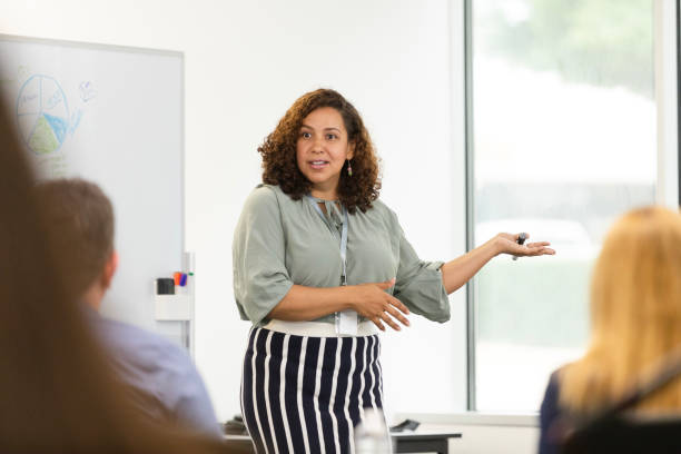 istock Female CEO gestures during presentation to unrecognizable employees 1603237299