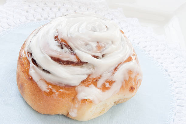 シナモンロールで覆われた光沢のあるクリーム、ブルーのレースの敷物 - cinnamon bun icing pastry ストックフォトと画像