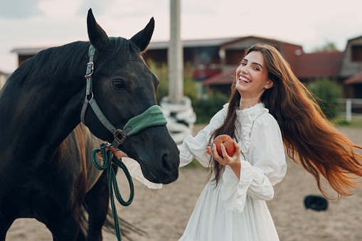 Woman laughing feeds her horse apple at outdoors ranch
