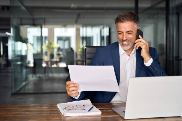 istock Focused Hispanic businessman doing paperwork in office with copy space. Happy Latin or Indian male business man holding documents, working at laptop computer doing online trade market tech research. 1603245523