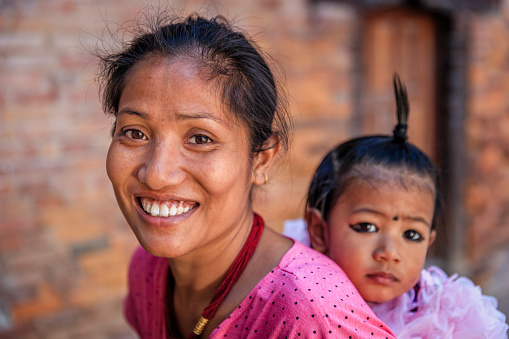 Nepali young mother carrying her little daughter in Bhaktapur. Bhaktapur is an ancient town in the Kathmandu Valley and is listed as a World Heritage Site by UNESCO for its rich culture, temples, and wood, metal and stone artwork.